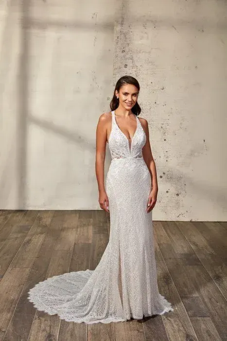 Bride in a beaded white gown with a plunging neckline, standing in a neutral-toned room.