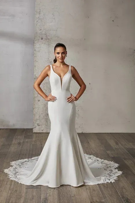 Woman in a white mermaid wedding dress with a deep V-neck, hands on hips, posing in a studio.