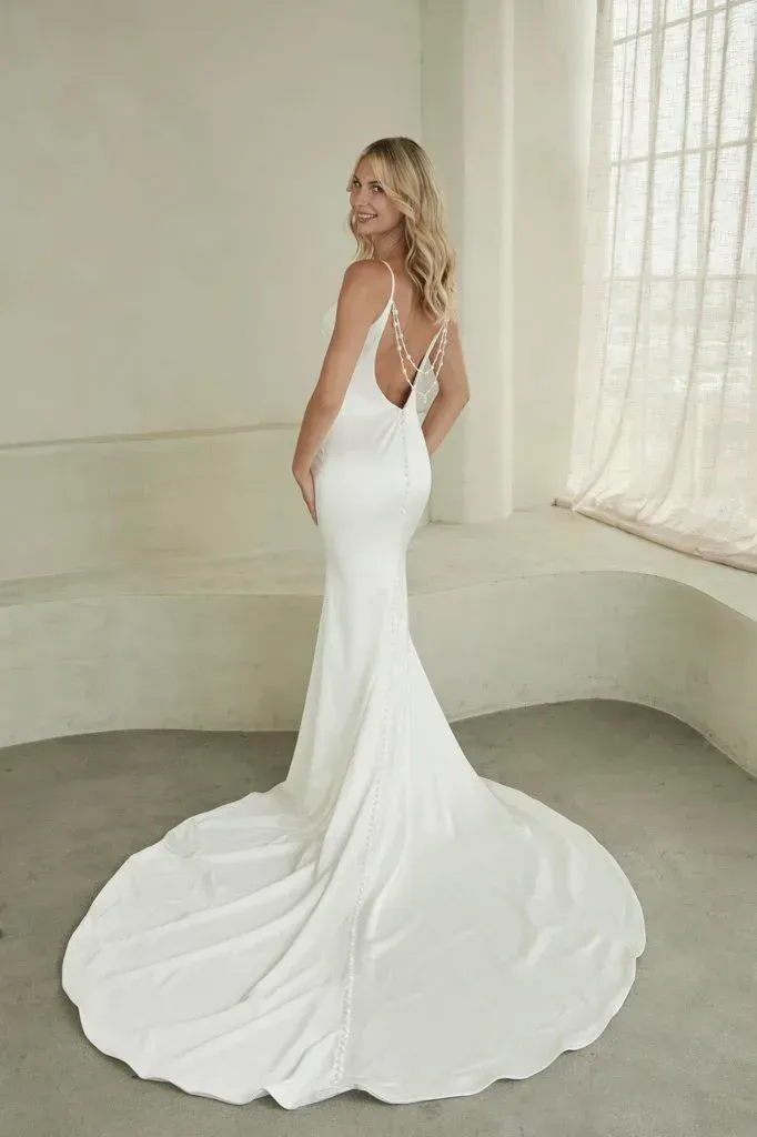 Blonde woman in a white wedding gown with a long train poses in front of a window.