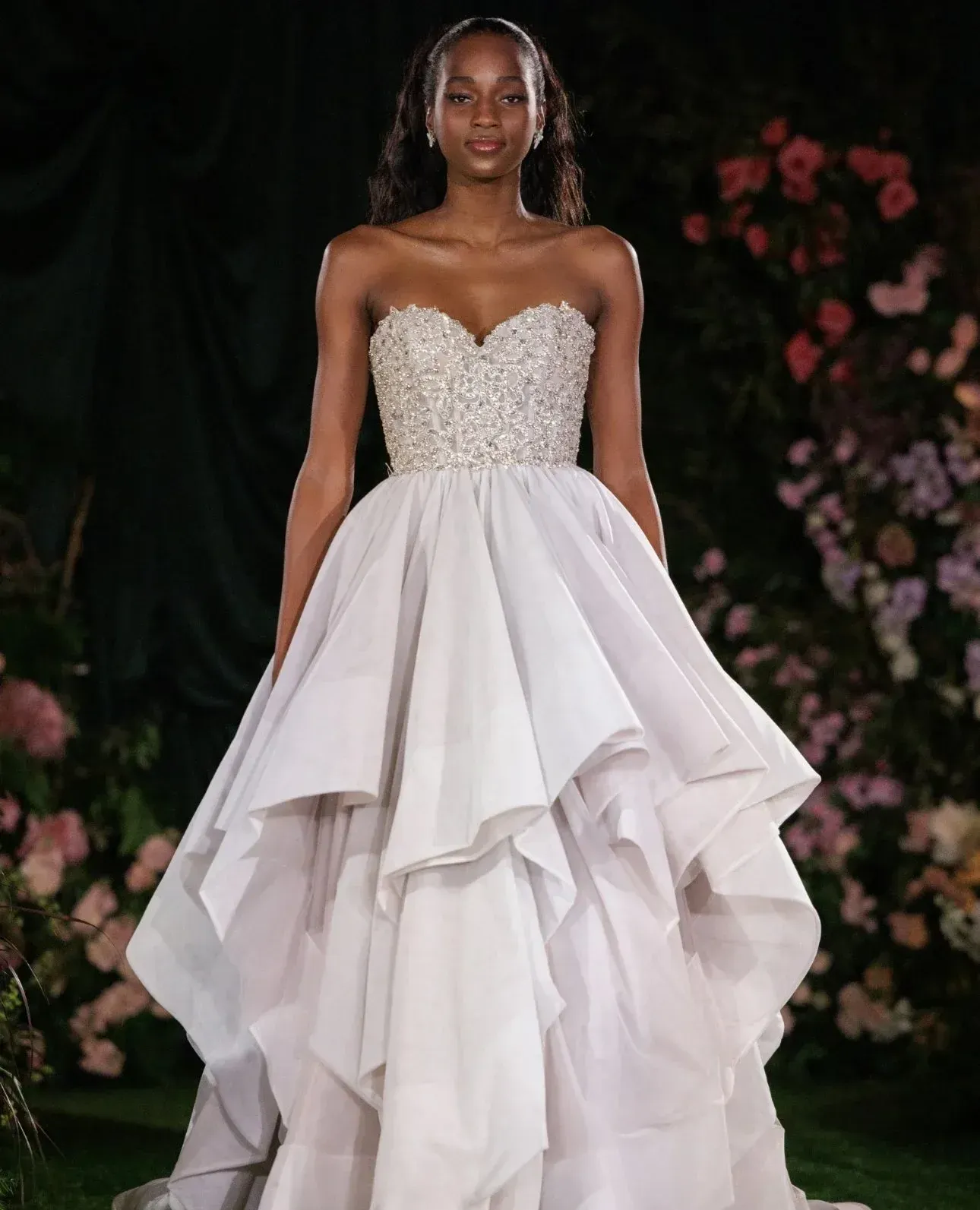 Woman in strapless wedding dress with embellished bodice and layered skirt, outside with flowers.