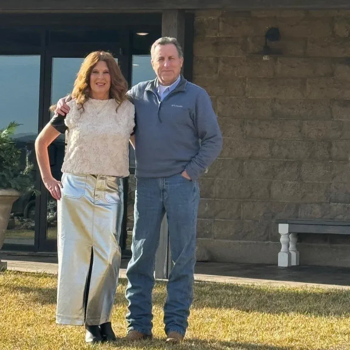 Woman in silver outfit and man in blue jeans stand together in front of a building.