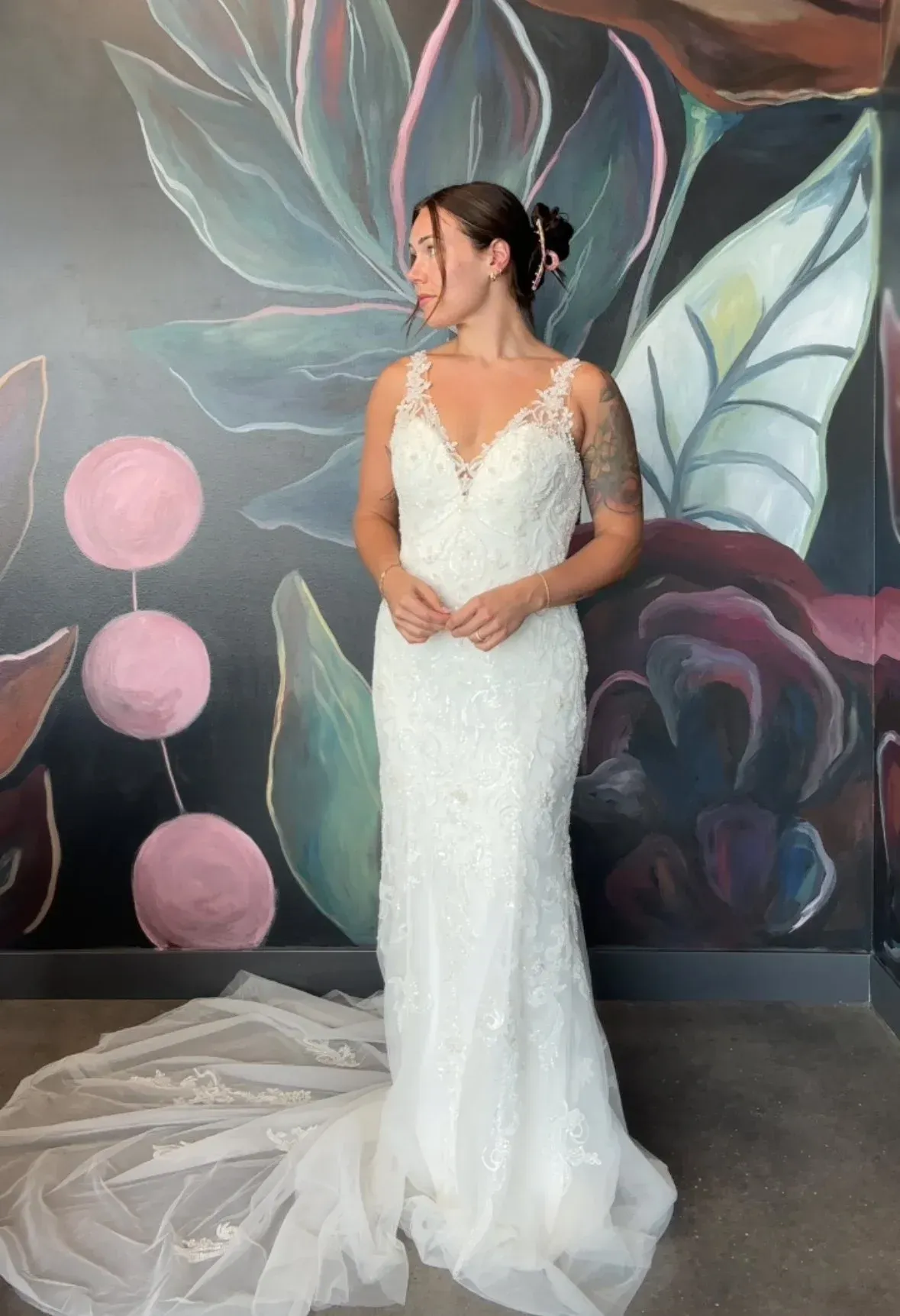 Bride in a white wedding dress with floral detail, standing in front of a mural.
