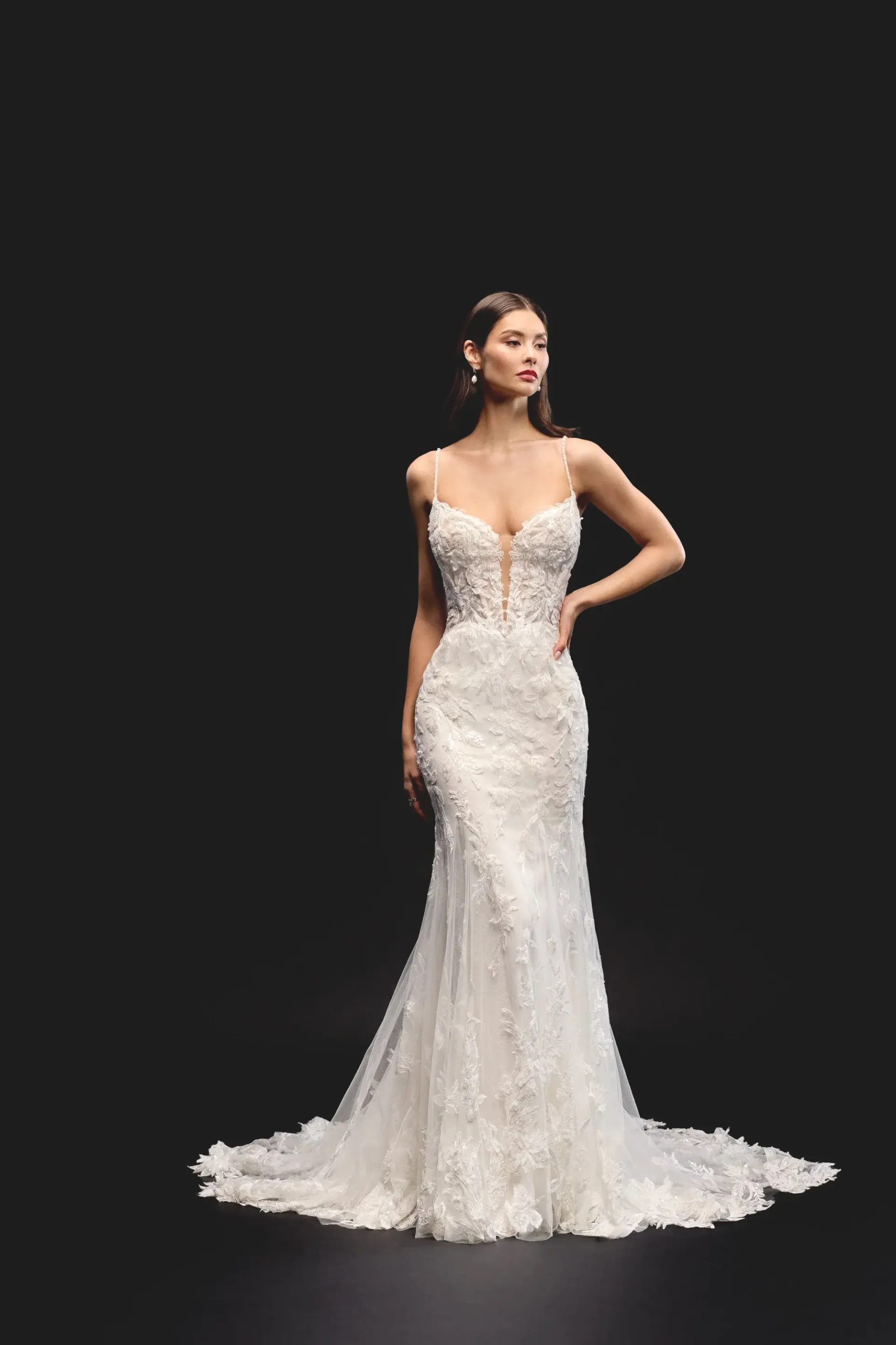 Woman in white embellished wedding gown poses against a dark background.