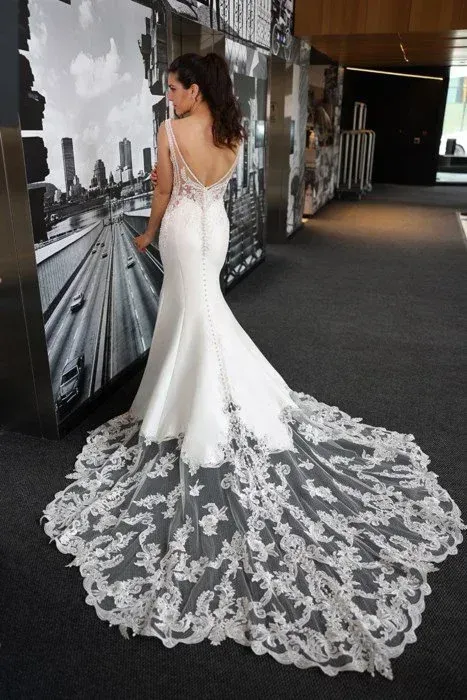 Woman in white wedding gown, back view. Dress features a low back and long lace train.