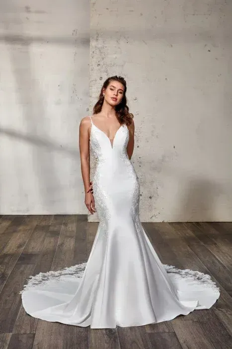 Woman in a white mermaid wedding dress with a plunging neckline, standing in front of a neutral wall.