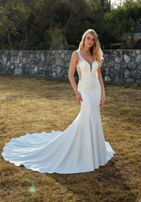 Blonde woman in a white wedding dress with train, standing outdoors.