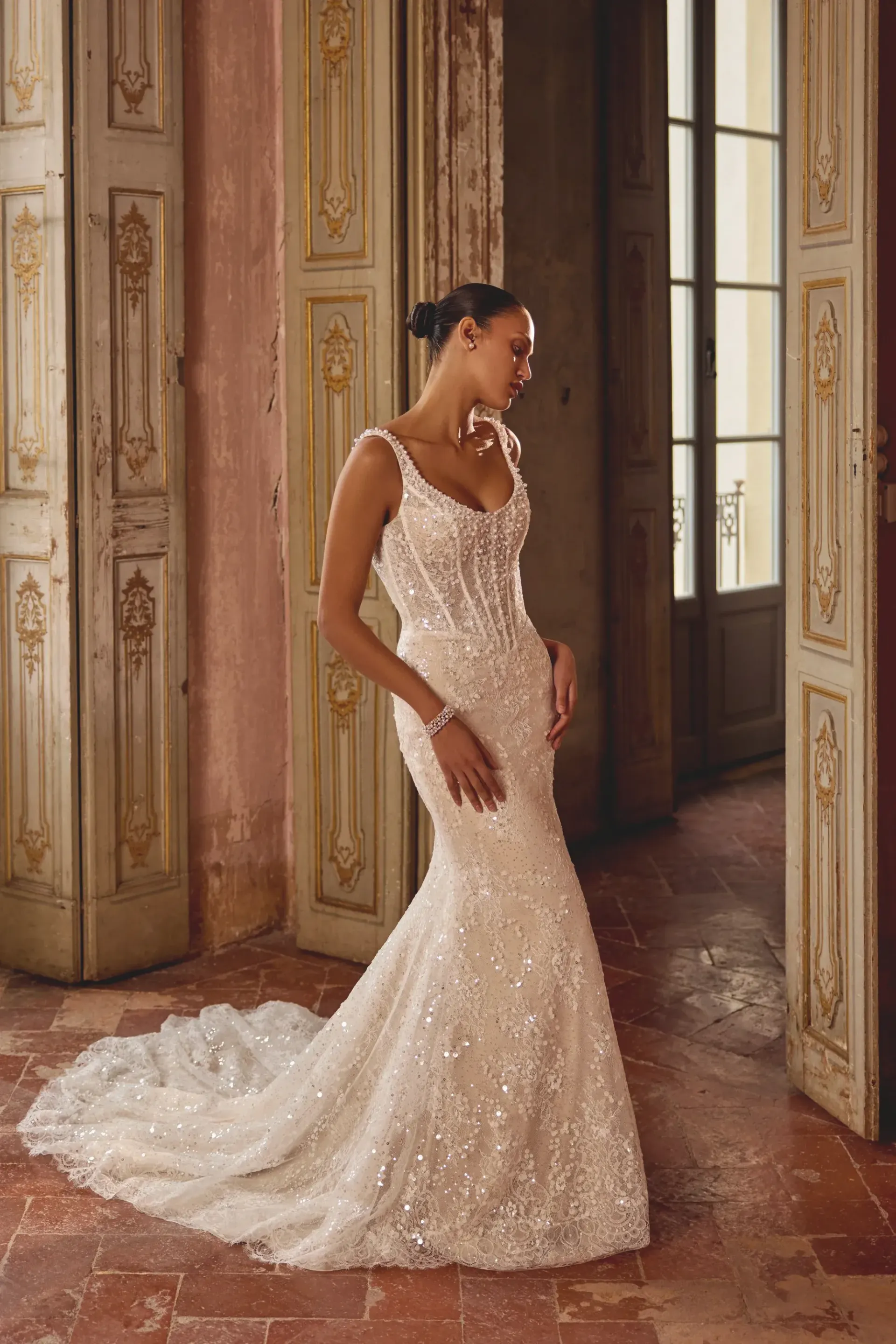 Woman in a sparkling wedding dress with a train, standing in a vintage doorway.