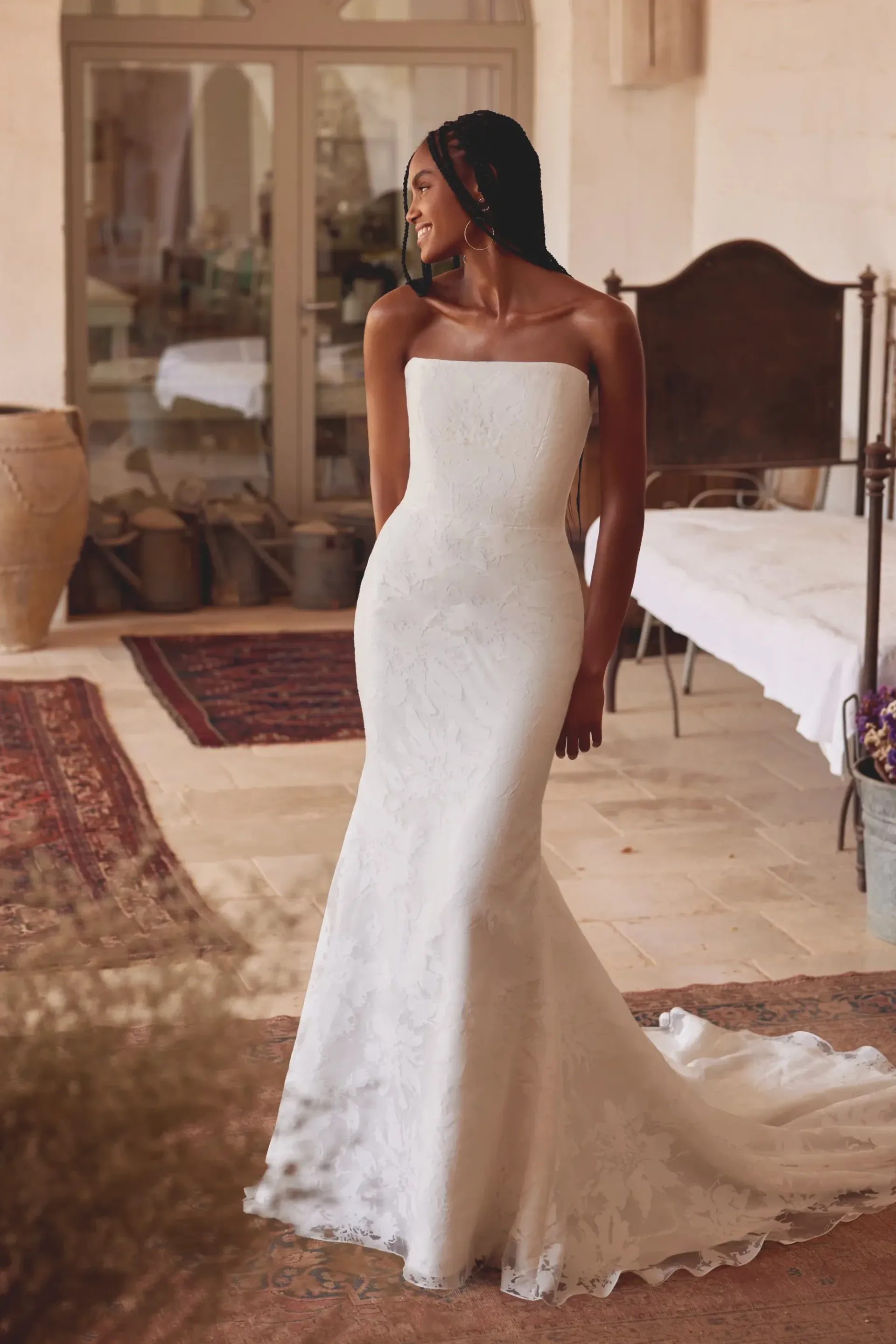 Woman in white strapless lace wedding dress, smiling, standing outdoors.