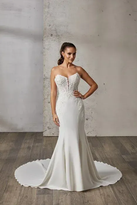 Woman in a strapless white mermaid wedding dress with floral detailing, posing indoors.