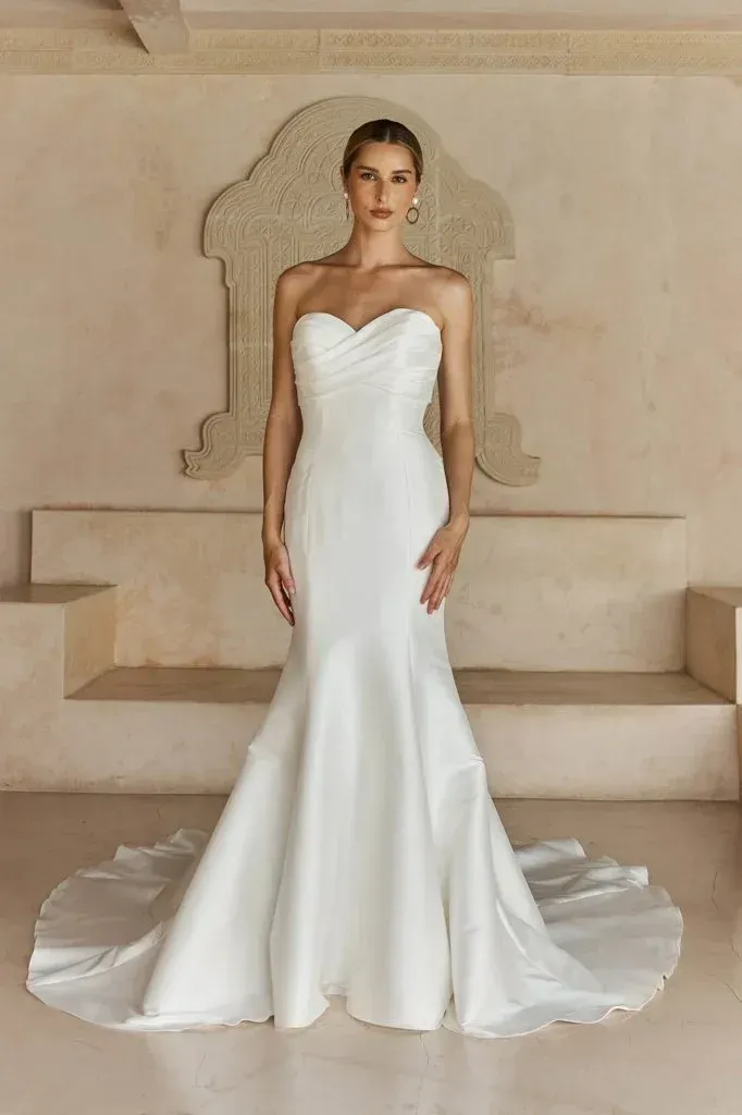 Woman in strapless white mermaid wedding dress, standing in front of a decorative archway.