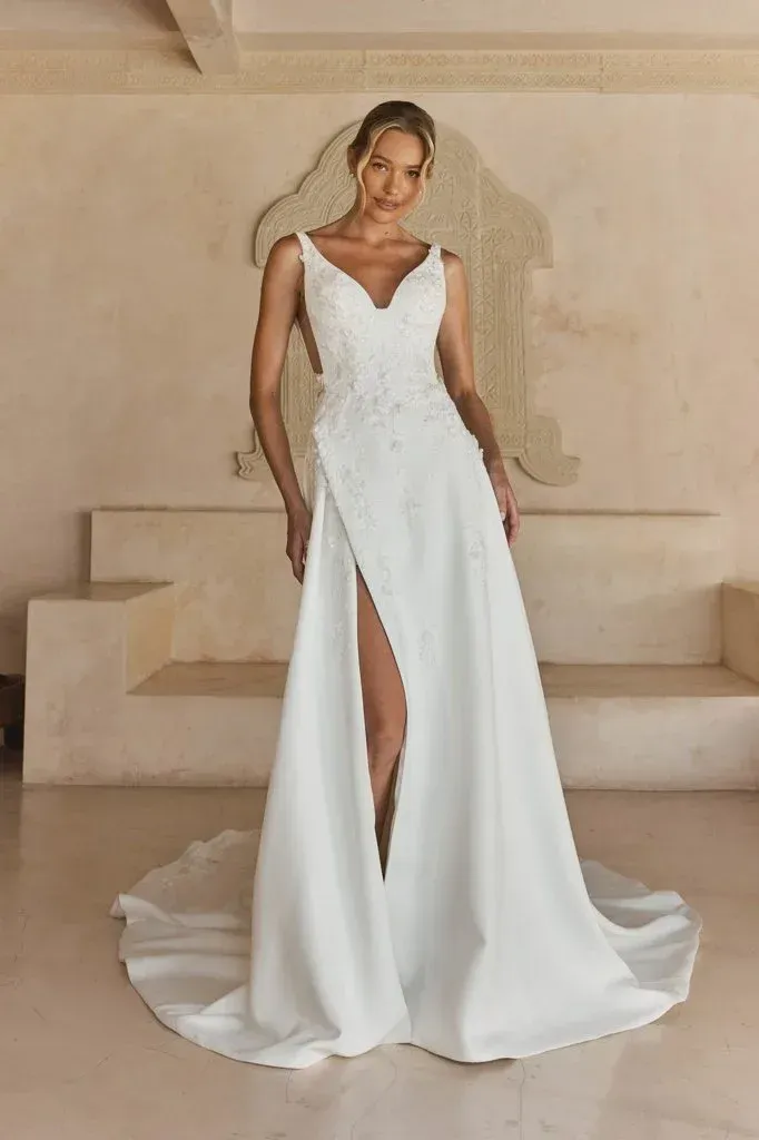 Woman in white wedding dress with a high slit, standing indoors.