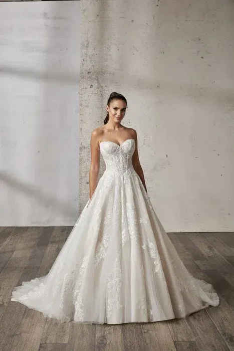 Woman in a strapless white wedding dress smiles in front of a textured gray wall and wood floor.