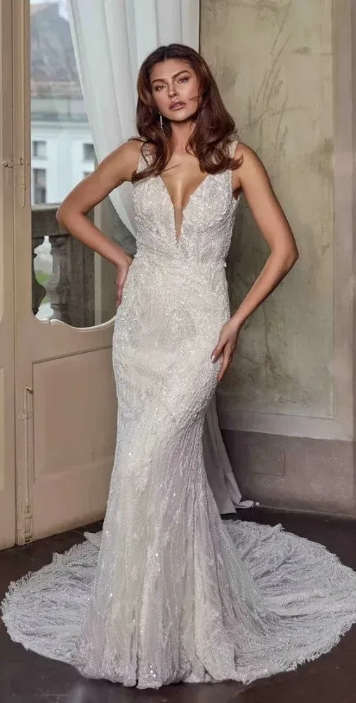 Woman in beaded white wedding dress, deep V-neckline, with train. Posing inside doorway.