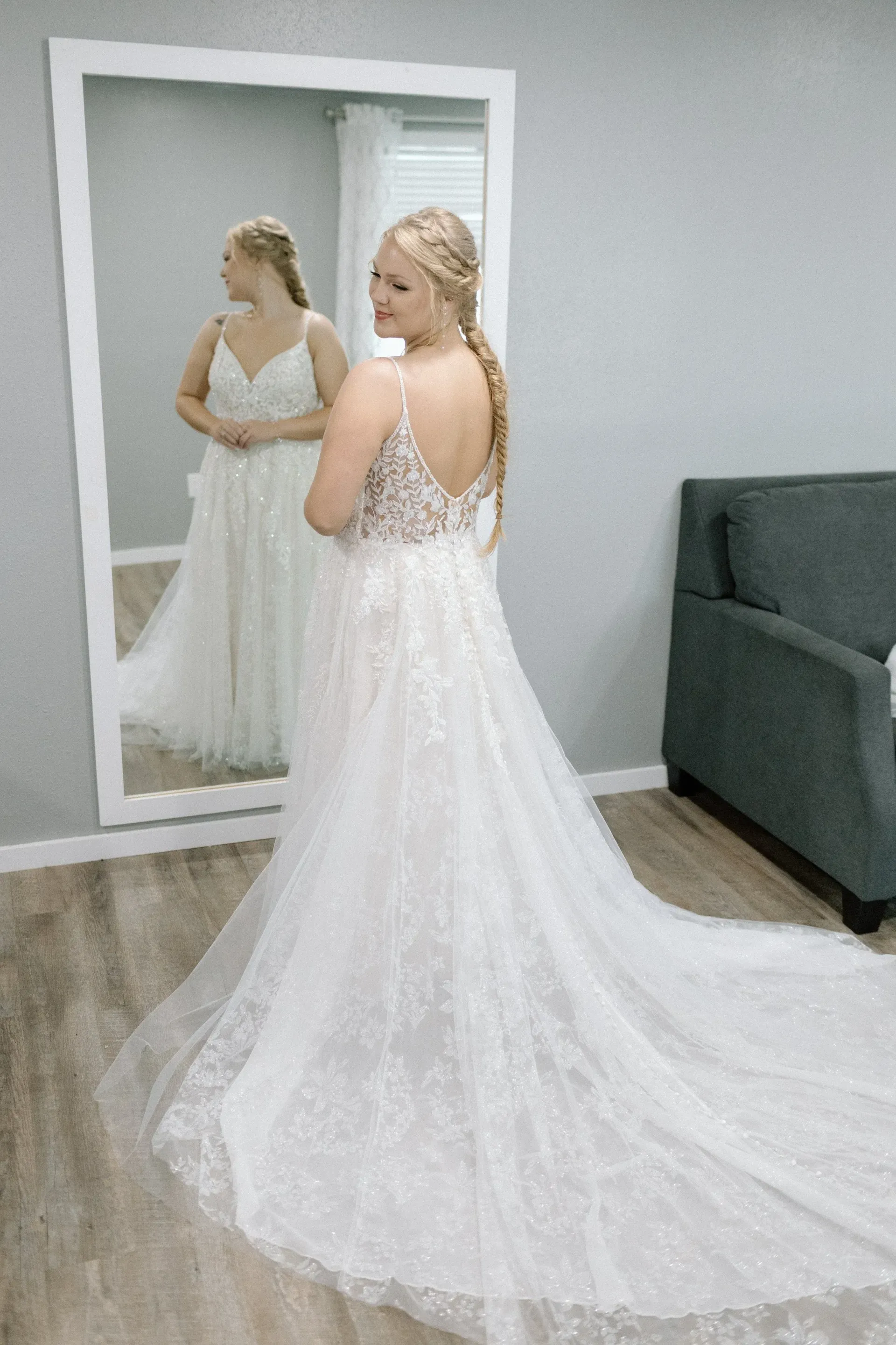 Woman trying on a sparkling white wedding dress in front of a mirror; indoor setting.