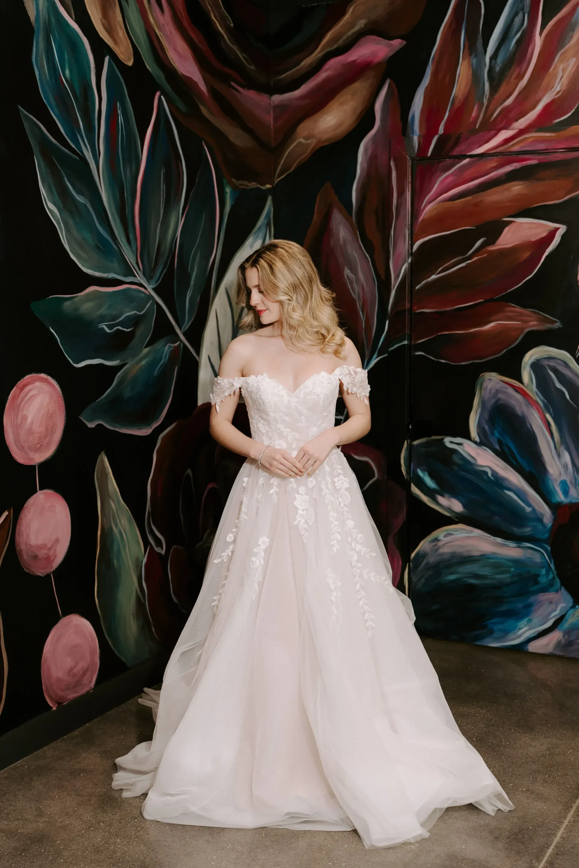 Woman in a blush wedding dress poses in front of a floral mural.