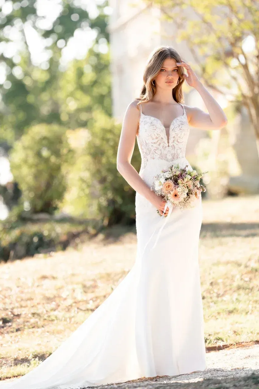 Bride in white dress, holding flowers, standing outdoors.