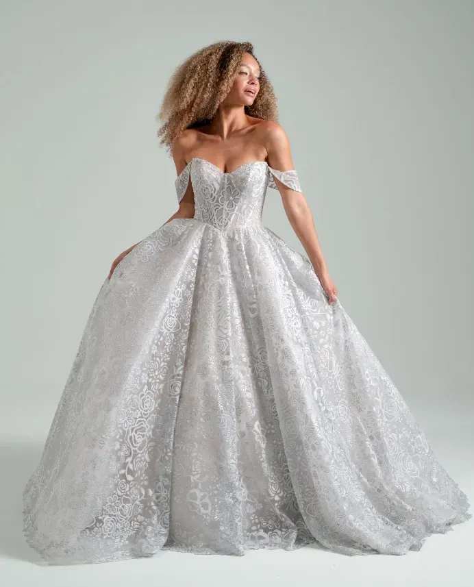 Woman in a sparkly, off-the-shoulder silver ballgown poses against a light grey backdrop.