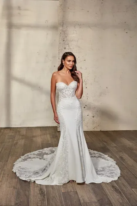 Woman in a strapless white wedding dress with a long train, posing indoors.