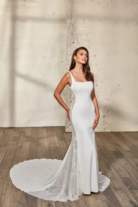 Woman in a white wedding dress with a train, posing in a studio.