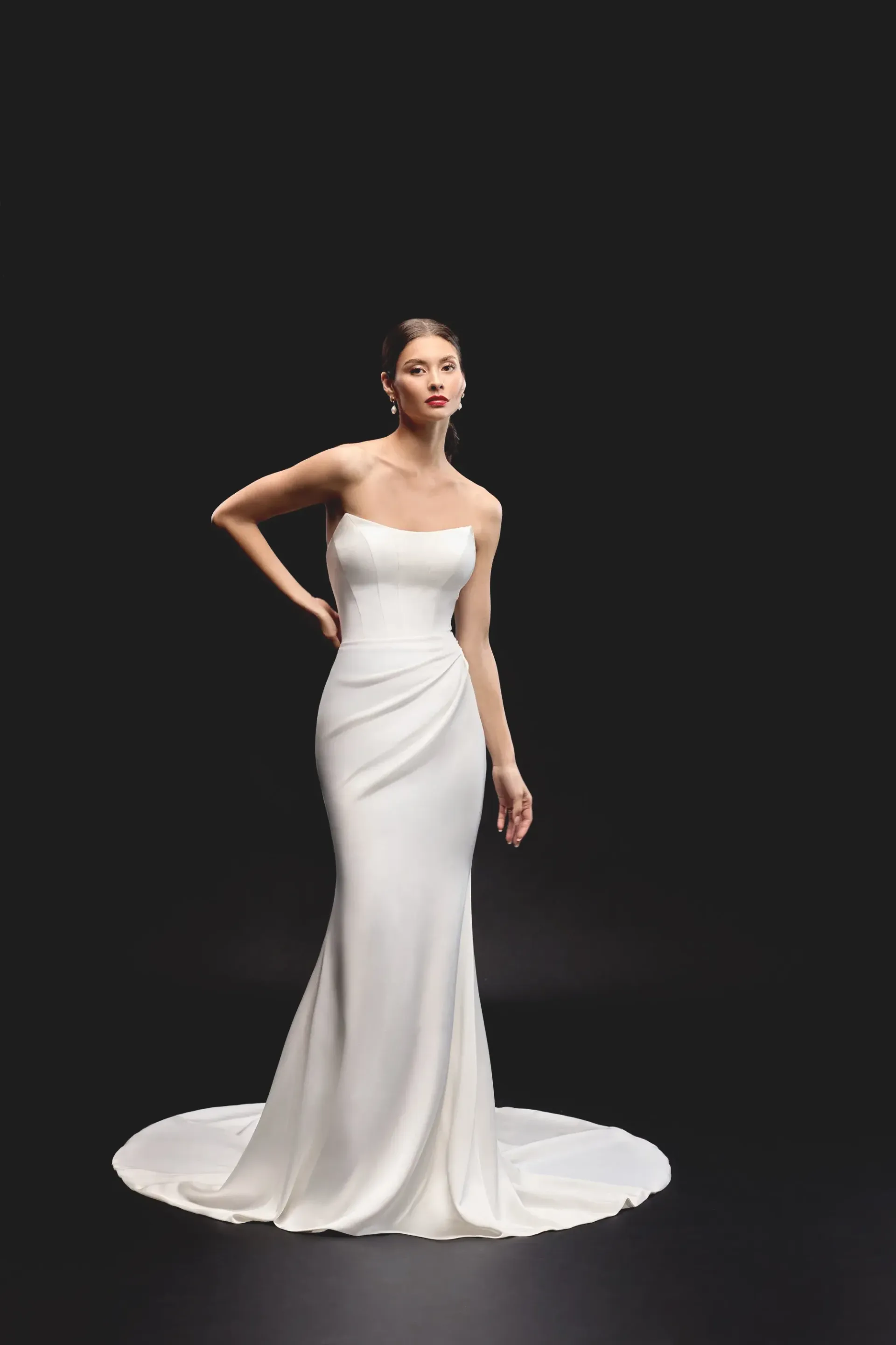 Woman in a strapless white wedding dress posing against a black background.