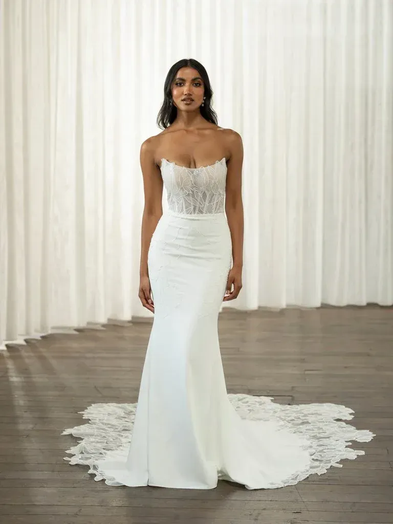 Woman in white strapless wedding dress, lace bodice, mermaid skirt, train, wooden floor.