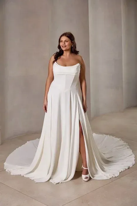Woman in a white strapless wedding dress with a thigh-high slit, posing indoors.