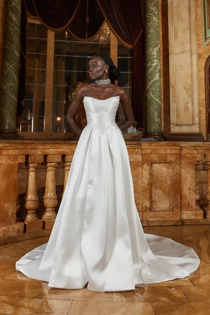 Woman in white strapless gown, posing in a grand hall with marble and gold accents.