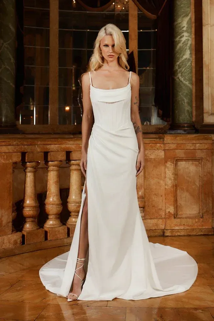 Woman in white wedding dress with high slit, standing in a grand room.