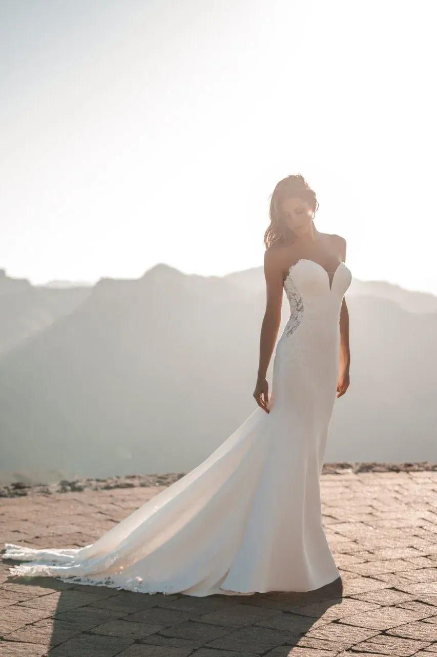 Bride in white strapless gown poses outdoors with mountains in the background.