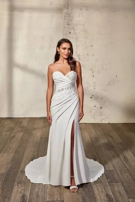 Woman in a white strapless wedding dress with a high slit, standing on wooden floor.