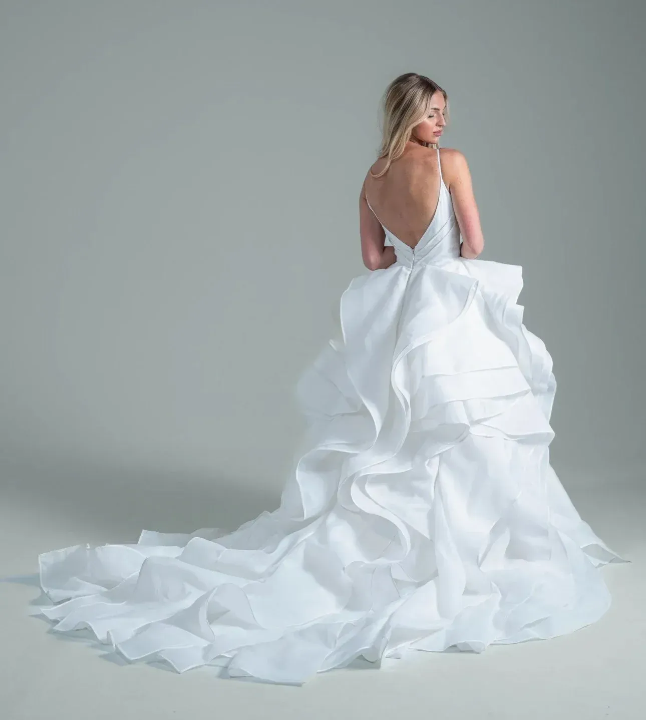 Blonde woman in a white wedding dress with a ruffled skirt and train, back view.