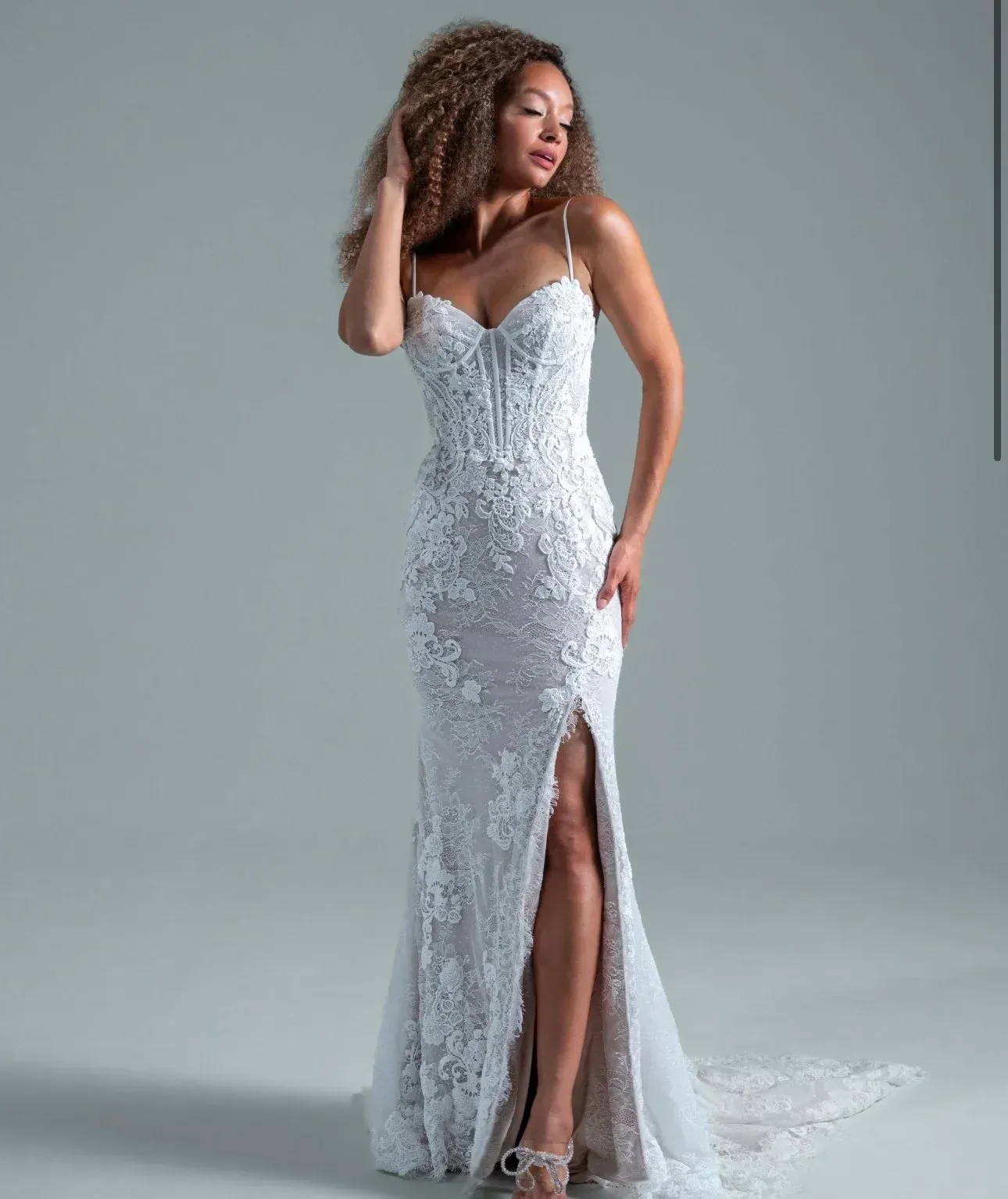 Woman in a white lace wedding dress with spaghetti straps and a thigh-high slit.