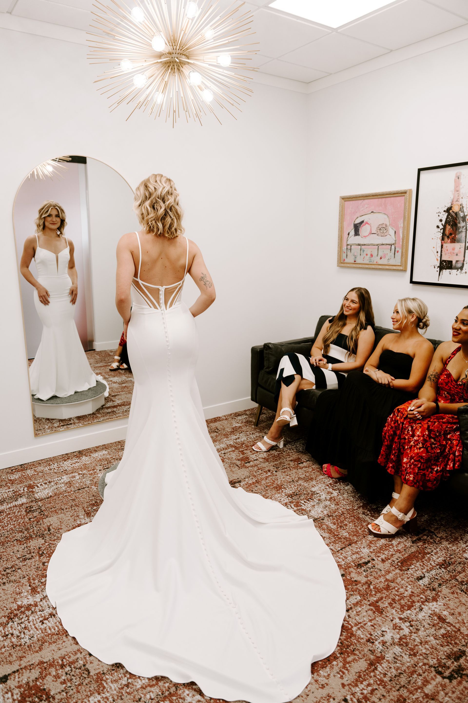 Bride trying on a white wedding dress in a bridal shop, surrounded by friends.