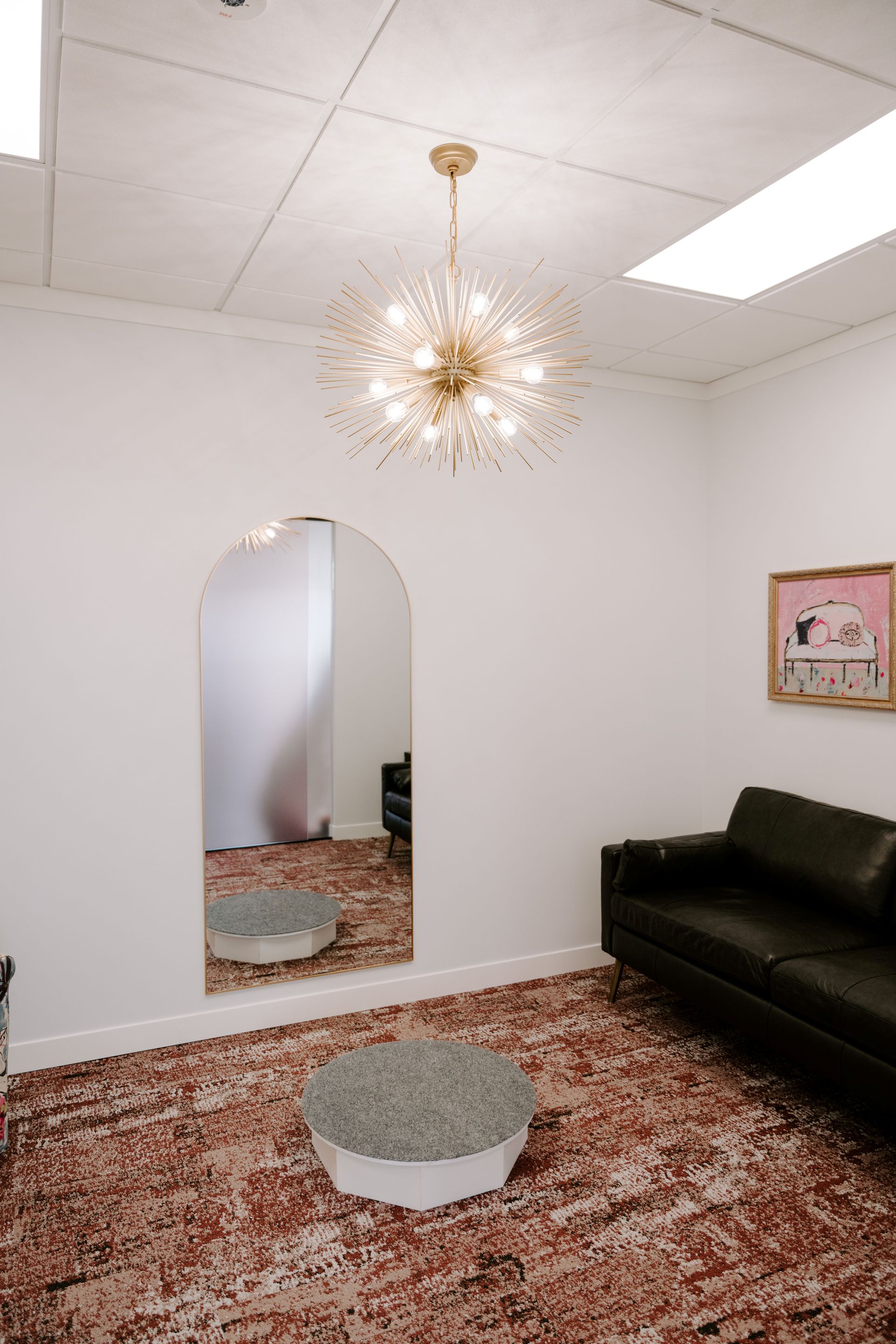 Room with a sofa, rug, round table, large mirror, and a starburst chandelier.