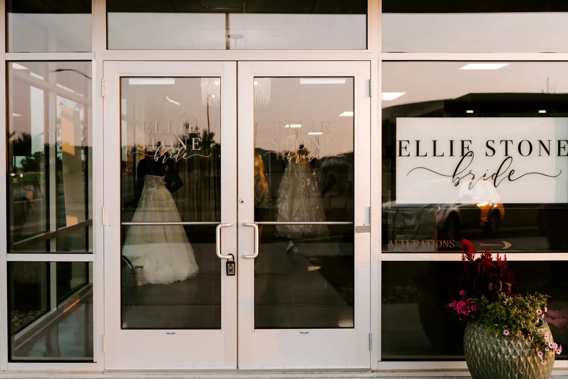 Exterior of Ellie Stone Bride store, glass doors with two wedding dresses, sign, and potted plants.
