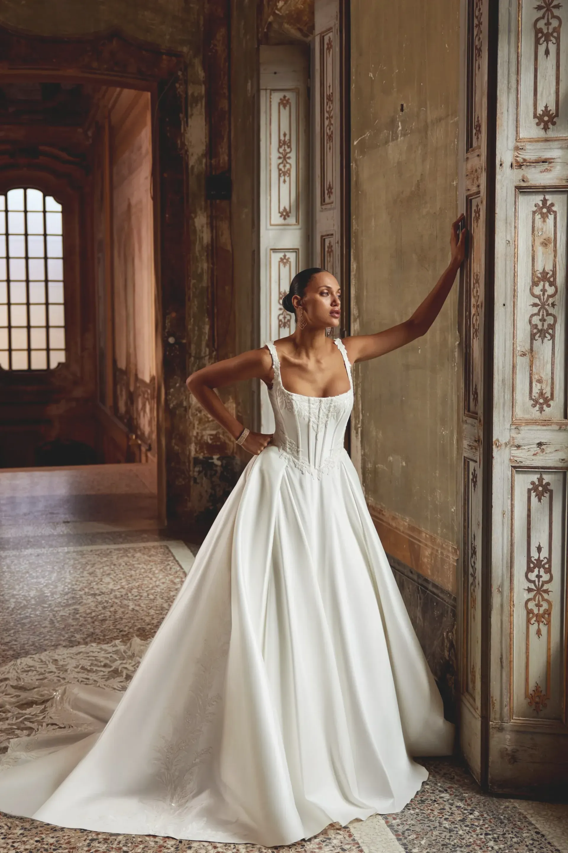 Woman in a white wedding gown poses in an ornate hallway.