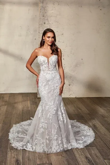 Woman in white lace strapless wedding dress, mermaid silhouette, poses with hands on hips, in a studio.