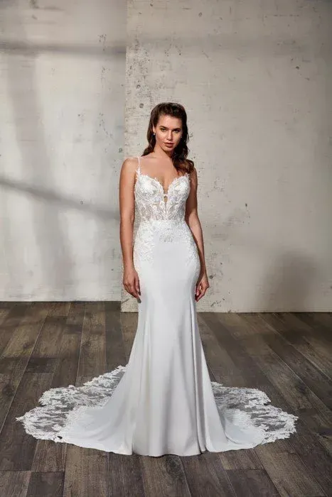 Woman in a white wedding dress with lace bodice and train, standing on wood floor.