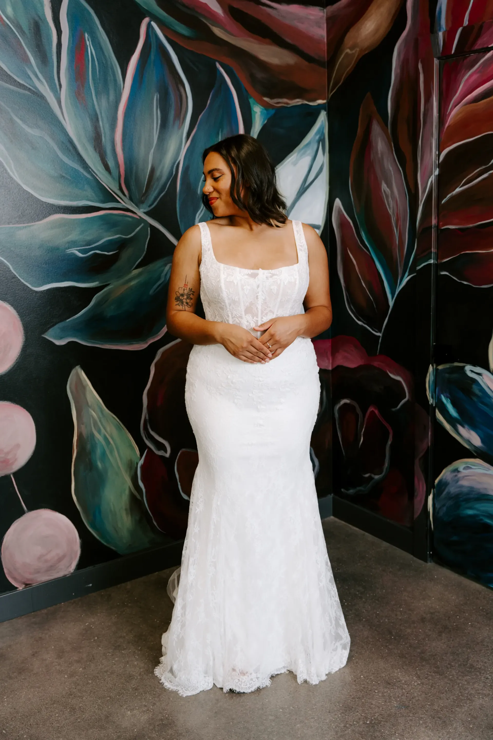 Bride in white wedding dress smiling in front of floral mural.
