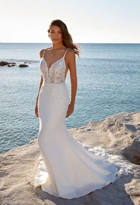 Woman in a white wedding dress stands on a rocky coast, ocean background.