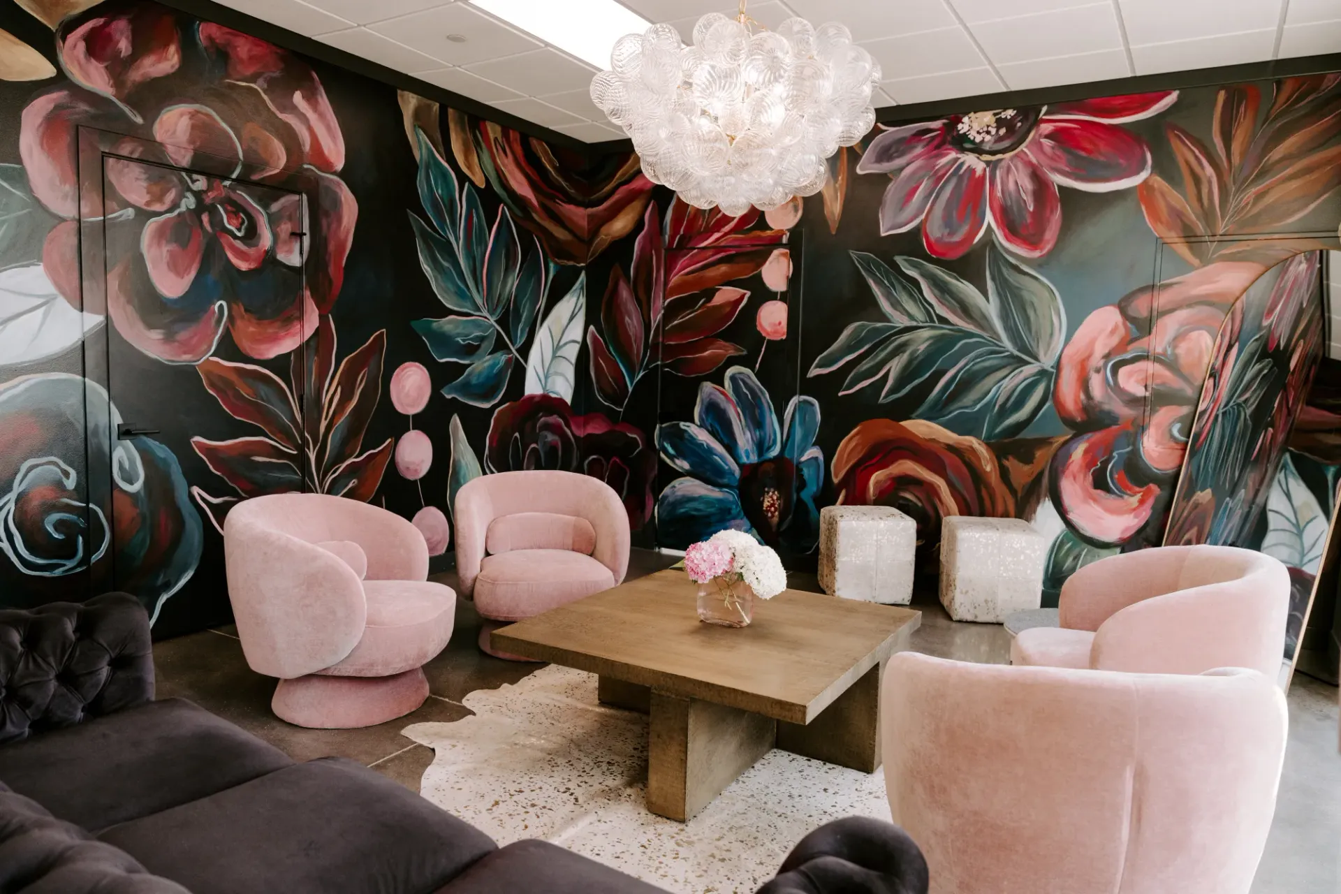 Cozy seating area with pink chairs, floral mural, and a chandelier.