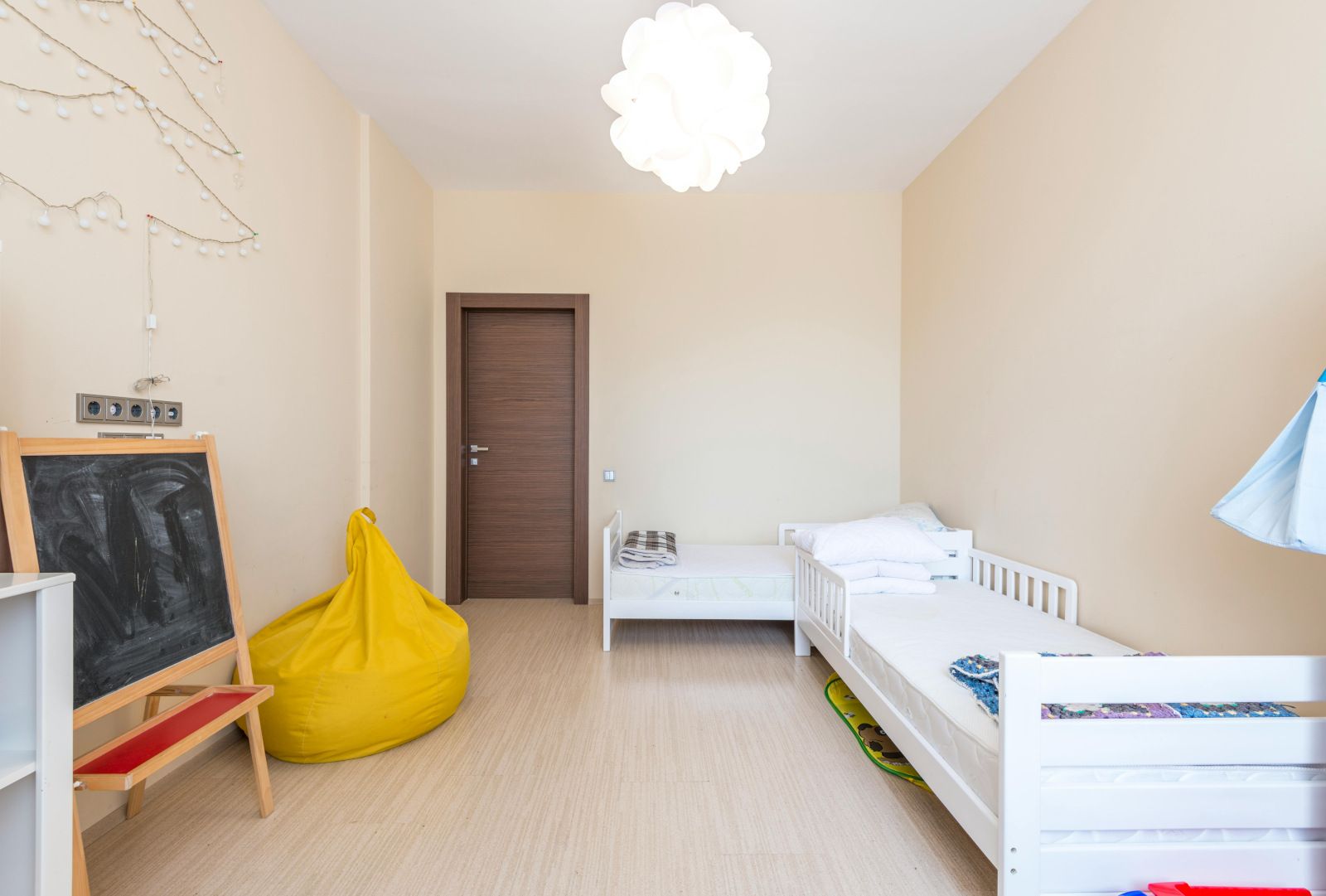 A bedroom with two beds , a bean bag chair and a chalkboard.
