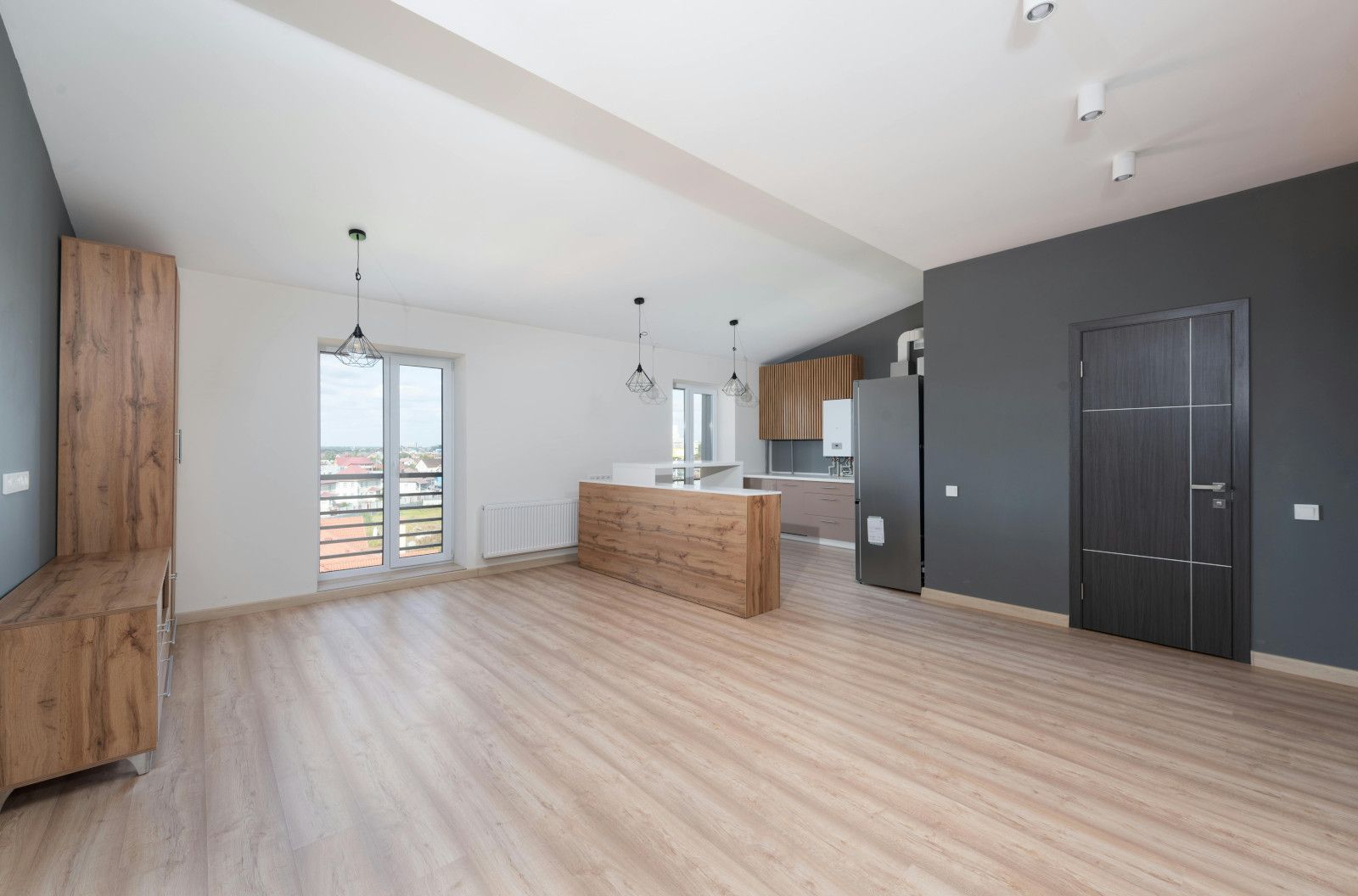 An empty living room with hardwood floors and a kitchen in the background.