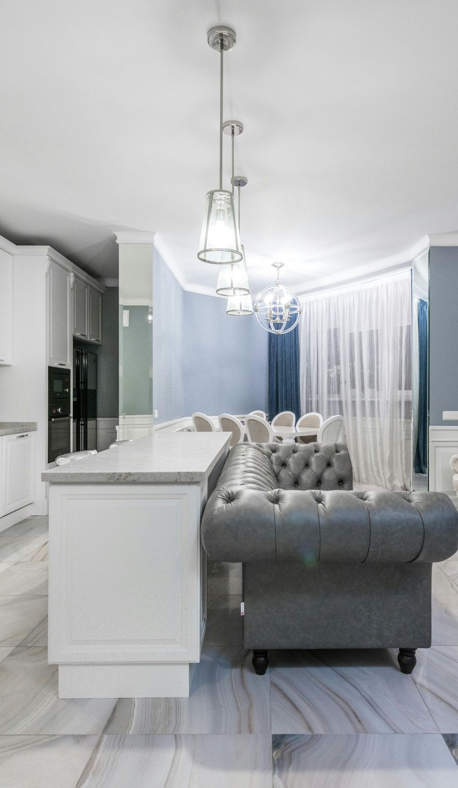 Gray tufted sofa, white kitchen island, and hanging lights in a modern living space with blue walls.