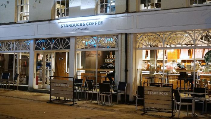 A starbucks coffee shop with tables and chairs outside at night.