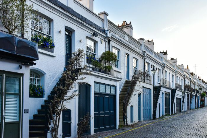 A row of white houses with stairs leading up to them on a cobblestone street.