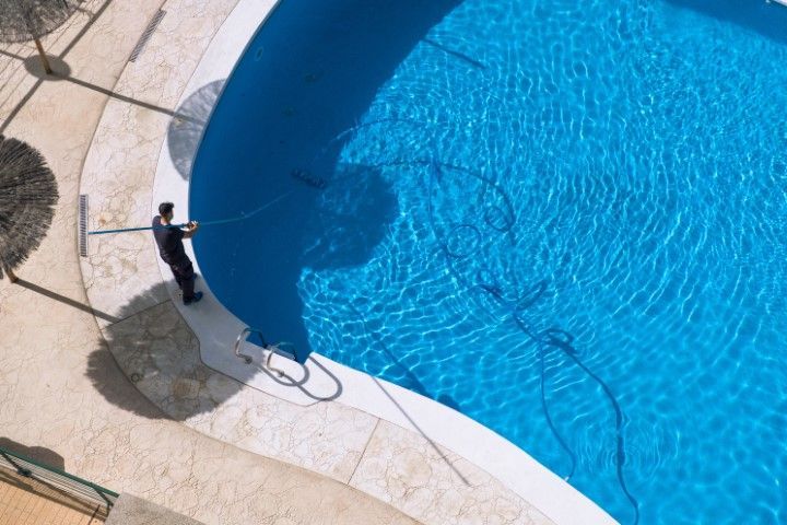 Person cleaning the edge of a blue swimming pool on a tiled patio