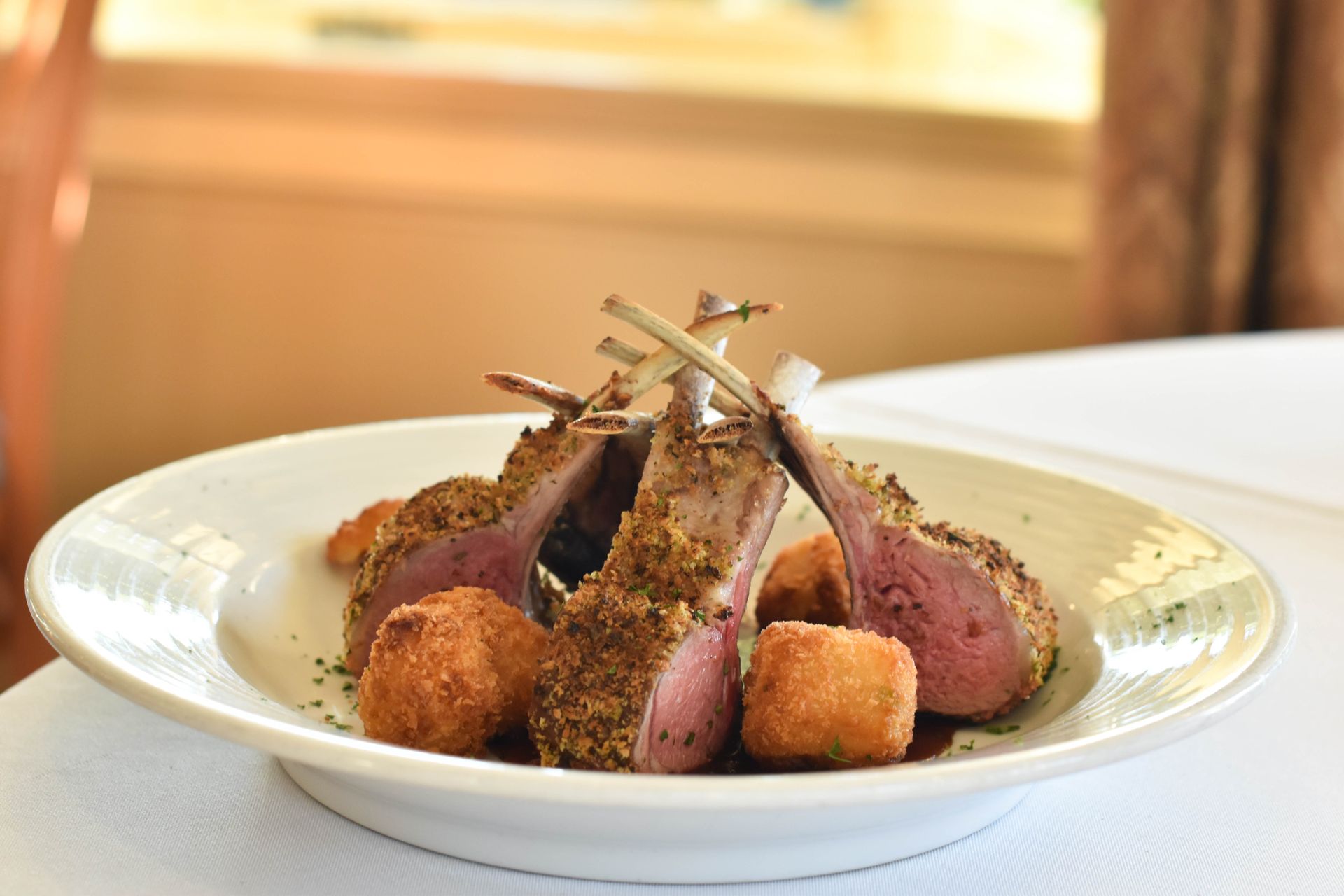 A white plate topped with lamb chops and potatoes on a table.