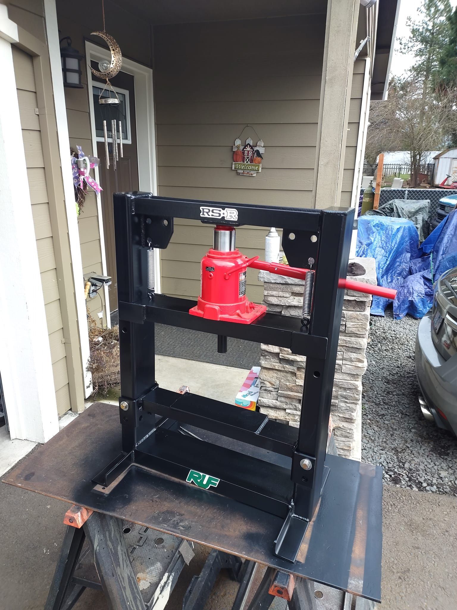 A hydraulic press is sitting on a table in front of a house.