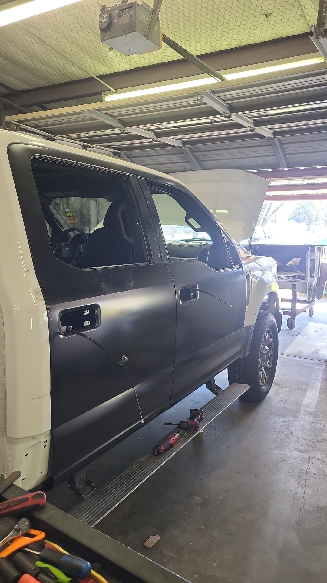 White and black pickup truck in a repair shop. The black door is being replaced.